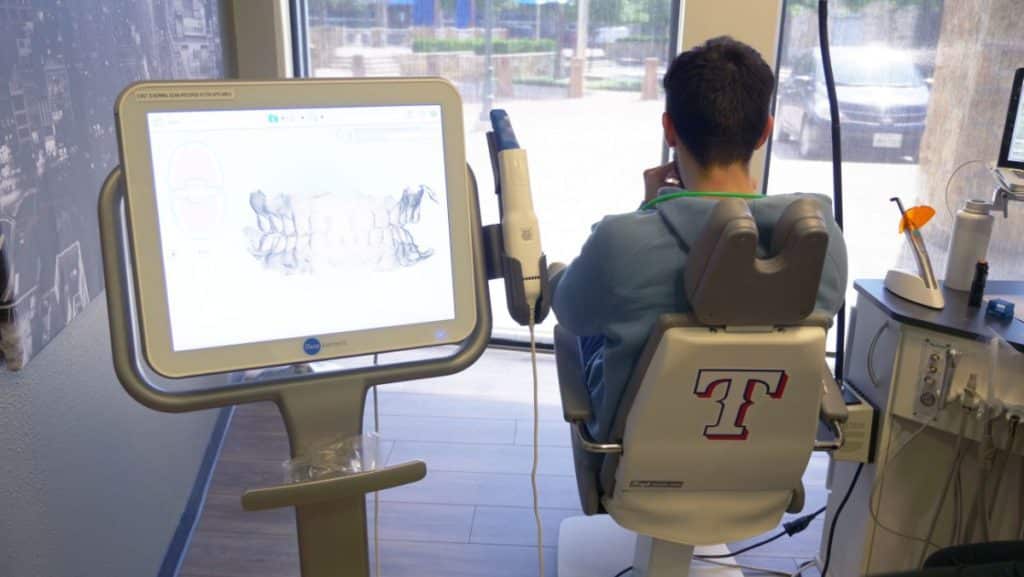 Patient sitting in dental chair with his back to the camera and xrays showing
